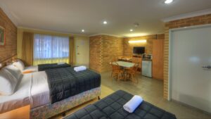 Queen bed with dark quilt and sitting area at the Jumbuck Motor Inn