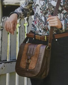 Tan crossbody saddle bag worn with a paisley shirt from Sherelle Fashions