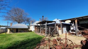 Grounds of Centenary Cottage Museum with open-sided sheds of vintage farm machinery