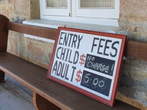 Hand-painted entry fees sign on a bench at Centenary Cottage Museum