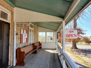 Verandah of Centenary Cottage Museum with timber pews and an Open sign