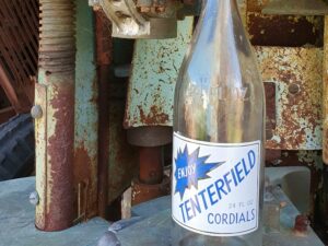 Antique Tenterfield Cordials bottle among rusted machinery at Centenary Cottage Museum