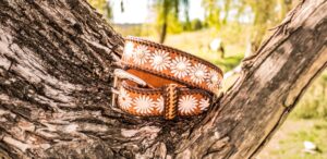 Hand-tooled leather belt resting on a weathered branch, Matilda Made Leather