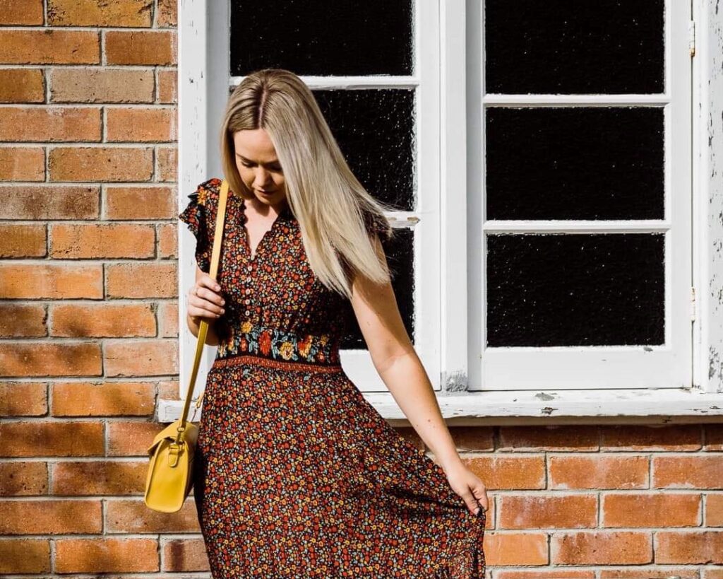 Model in a brown floral dress with mustard handbag outside Sherelle Fashions