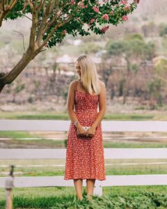 Model in a red ditsy-print dress by a white fence, Sherelle Fashions
