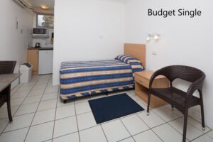 Budget single room with bed and wicker chair at the Tally Ho Motor Inn