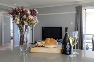 Open-plan living area with protea arrangement and sparkling wine at Carpe Diem Cottage
