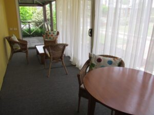 Enclosed verandah sitting area with cane chairs at Henry's Cottage