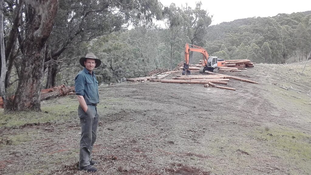 Highlands Logging operator standing before cleared timber and an excavator