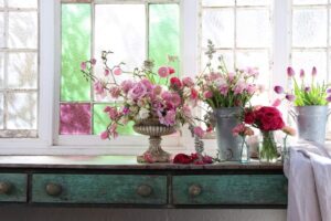Stained-glass window sill lined with vases of fresh blooms at White Cottage Flower Farm