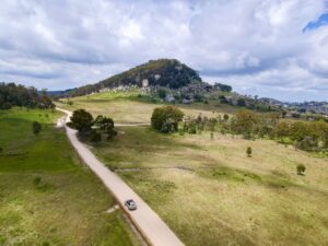 Aerial view of a country road winding past a rocky hilltop on the Historic Villages Loop near Tenterfield