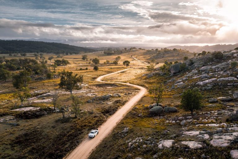 Car travelling a winding dirt road through granite country on Mount Mackenzie Drive at dusk