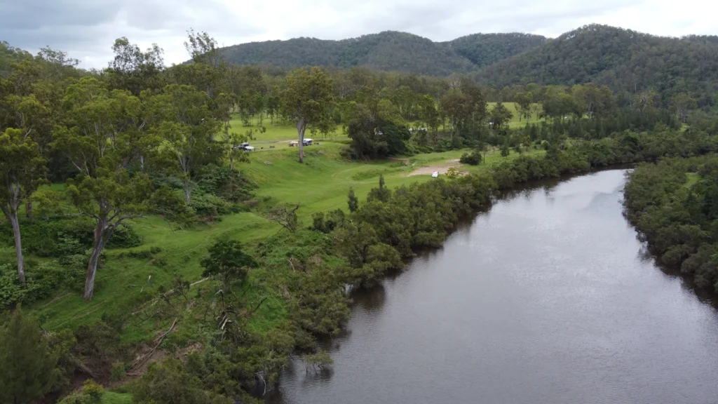 Aerial view of the open-field campground at On The Clarence Camping, nestled between the Clarence River and forested hills near Tabulam
